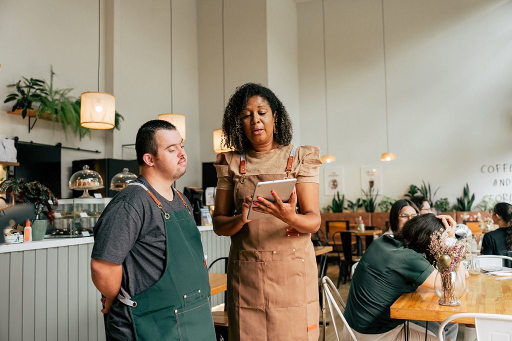 Cafe owner giving instructions to employee with Down syndrome